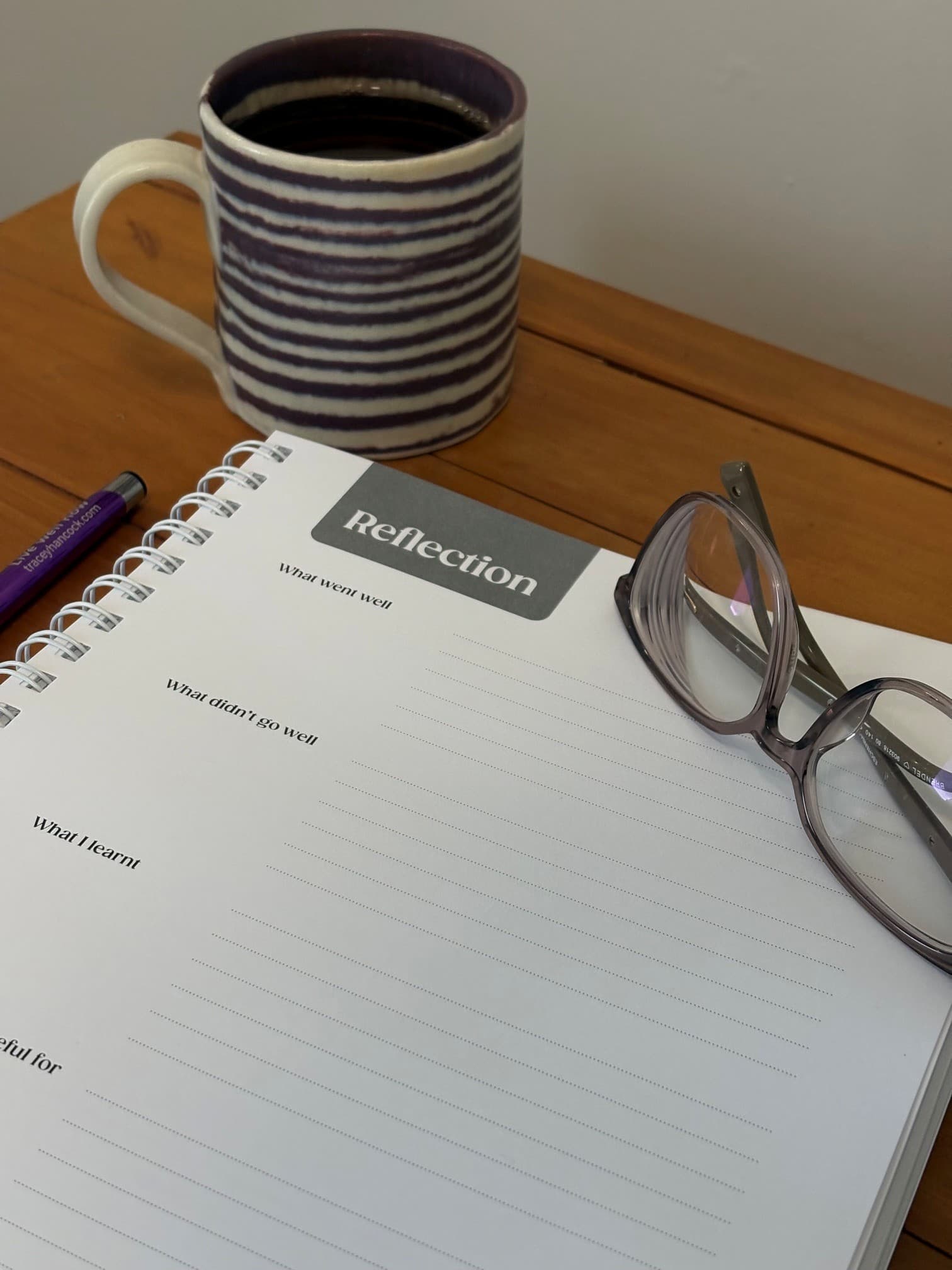 The Live Well Life Planner open on a cafe table beside a cup and glasses
