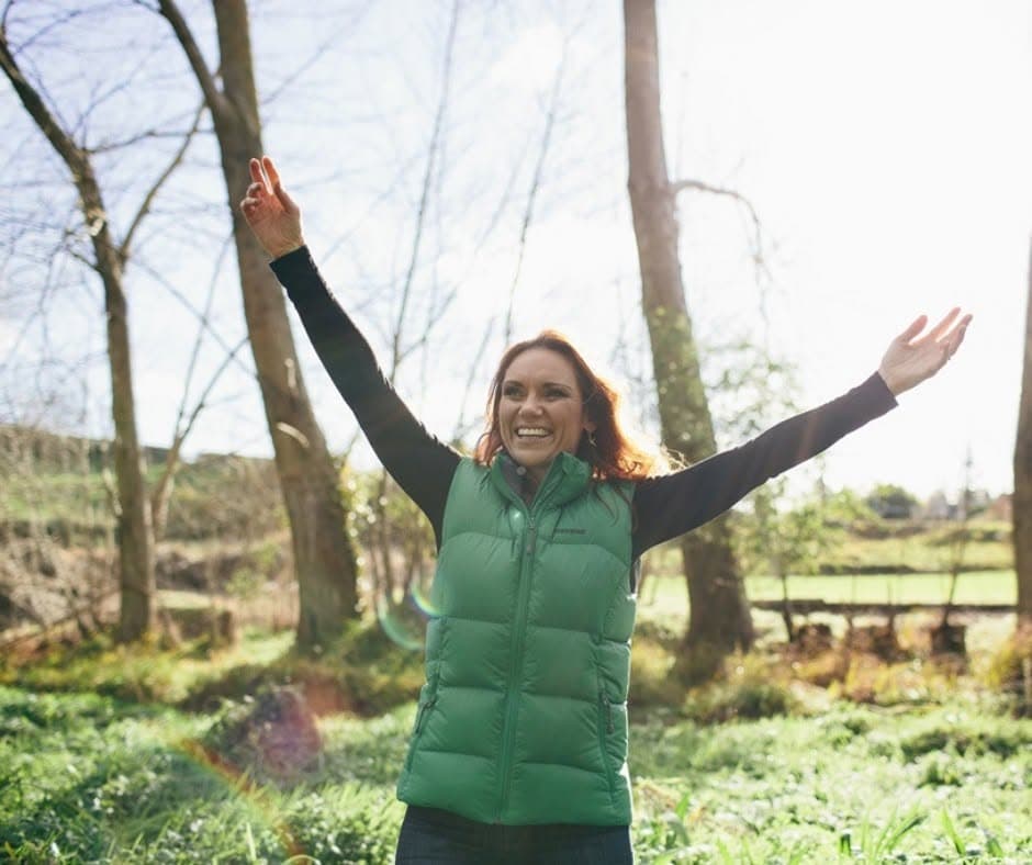Tracey Hancock with her arms raised in a field, free and joyful